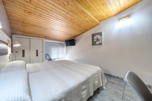 Dos camas en luminosa habitación abuhardillada de Hostal El Molino, Collado Villalba, con techo de madera y comodidades modernas