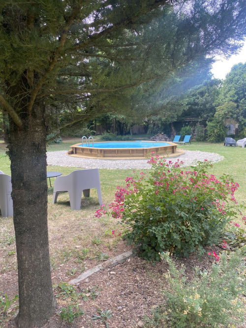 Le jardin Cocon De Curson avec piscine bleue, fleurs roses, arbres ombragés et transats blancs à Chanos-Curson