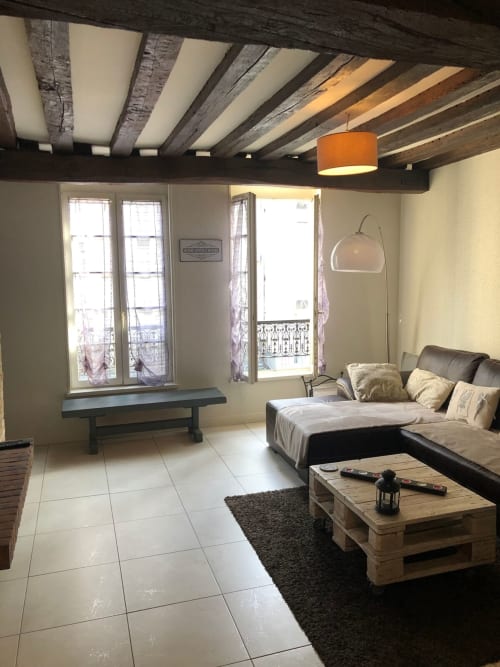 Spacieux salon d'appartement à Troyes aux poutres apparentes, mobilier moderne, fenêtres vue ville et confortable