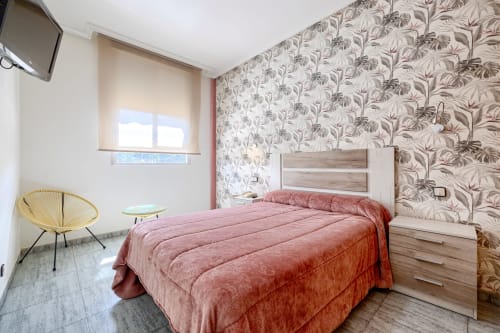 Habitación doble moderna en Hostal El Molino con ropa de cama rosa, papel tapiz floral y muebles contemporáneos