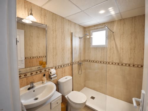 Baño moderno con paredes de azulejos beige, lavamanos, inodoro y ducha abierta en Apartamentos El Calón Playa