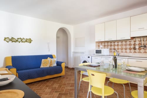 Appartamento moderno a Bari Sardo con divano blu, accenti gialli, tavolo da pranzo, cucina attrezzata e pavimento in cotto
