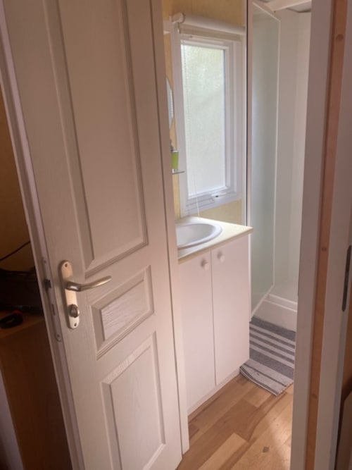 Salle de bain compacte du mobil-home villa Auvergne au Relais de La Mirpe, Bergerac avec vasque blanche, toilettes et fenêtre