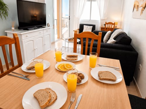 Mesa de desayuno con jugo de naranja, tostadas y galletas en Apartamentos El Calón Playa, Cuevas del Almanzora