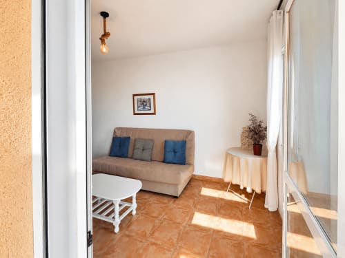 Cozy apartment living room at El Calón Playa with beige sofa, blue pillows, terracotta tiles, and natural light