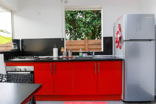 Cuisine moderne rouge avec plan de travail noir, électroménagers en acier inoxydable et vue jardin au gîte Kaz A Bibi à Sainte-Rose