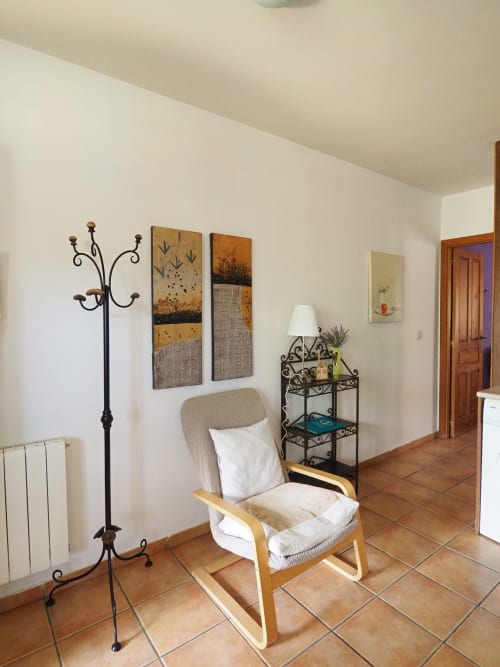 Acogedora sala de estar en apartamento rural español con mecedora, lámpara decorativa de pie y cuadros en pared de baldosas terracota