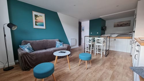 Modern apartment living area with teal accent wall, gray sofa, white bar seating, and open kitchen at Ô LOCH in La