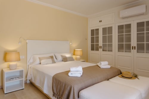 Luminoso dormitorio en Las Golondrinas con cama queen, mesilla blanca, paredes color crema y armarios empotrados en Cap d'Artrutx