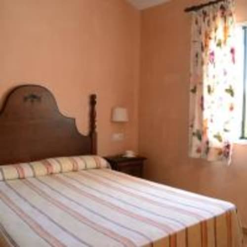 Acogedor dormitorio en villa Las Golondrinas, Cap d'Artrutx, con cama de madera, paredes melocotón y cortinas florales