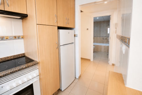 Cocina moderna en Apartamentos El Calón Playa con gabinetes de madera, refrigerador blanco, estufa eléctrica y espacio abierto