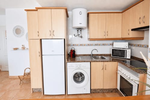 Modern kitchen in Apartamentos El Calón Playa apartment with light wood cabinets, white appliances, and granite countertops