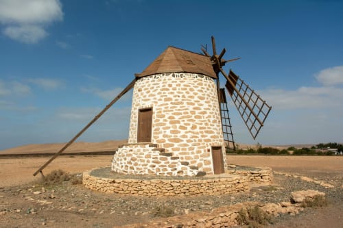 Ancien moulin à vent en pierre blanche avec ailes en bois dans le paysage désertique de Fuerteventura près de Corralejo