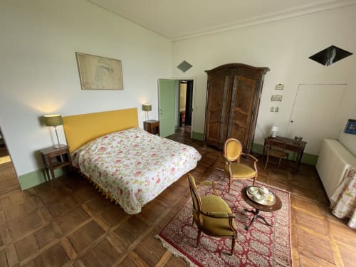 Chambre élégante au Château de Vaux Morvan avec tête de lit jaune, literie fleurie, armoire en bois et vue sur le jardin