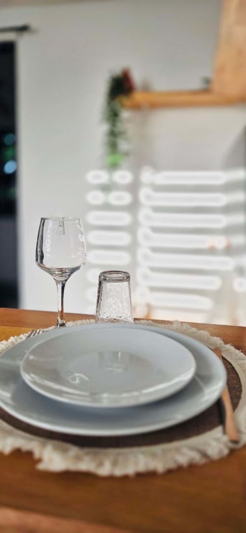 Mise en place élégante aux Maisons En Or : assiettes blanches, verre à vin et verre à eau sur table en bois dans l'appartement de Cayenne