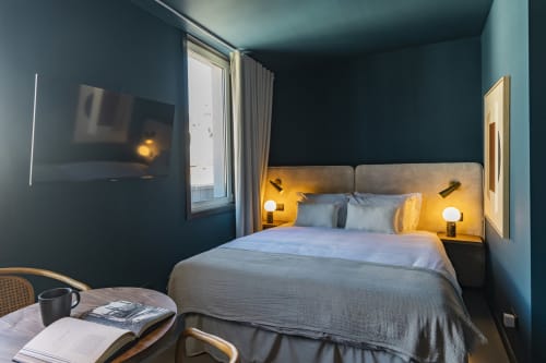 Estúdio compacto moderno em hotel no Porto com paredes azul-petróleo, cama queen, TV na parede e iluminação ambiente das luminárias de cabeceira
