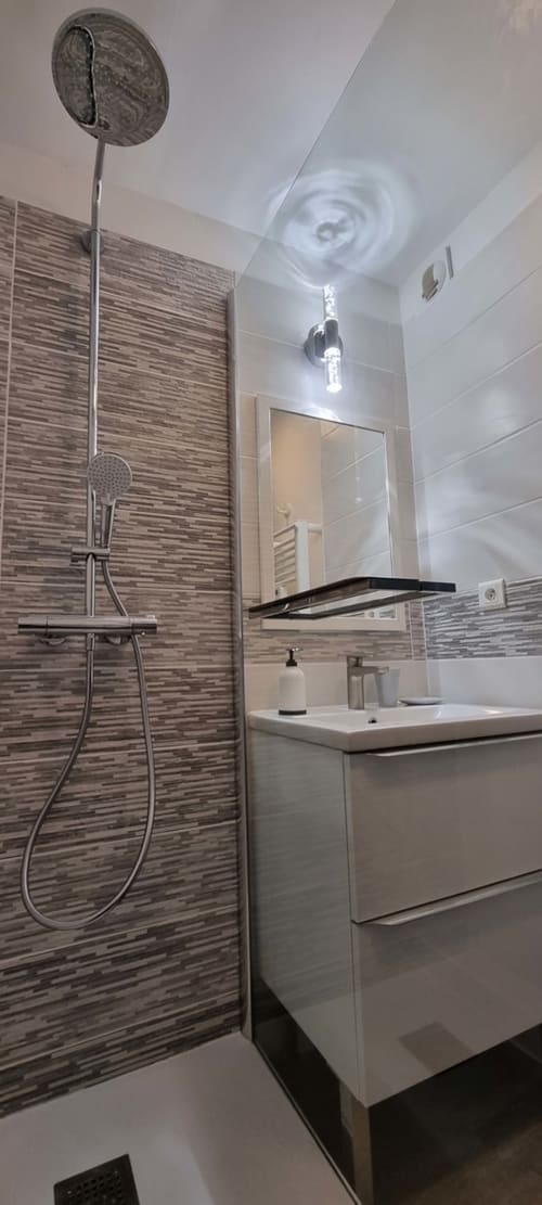Modern bathroom with striped tile shower, white sink vanity, mirror, and ceiling ventilation in Ô CAP COZ apartment at
