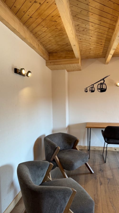 Modern lounge area with gray chairs, wooden beamed ceiling, and cable car wall art at La Ferme des Georgières