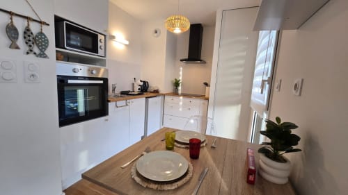 Modern apartment kitchen and dining area at Ô Kastel in La Fôret-Fouesnant with white cabinetry, wooden table set for dining,