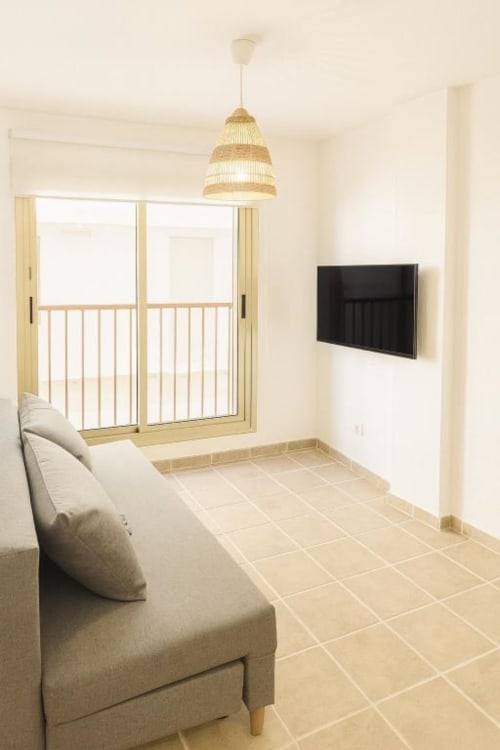 Sala de estar moderna con sofá beige, TV de pantalla plana, lámpara colgante tejida y vista al océano desde el balcón de El HierroStay