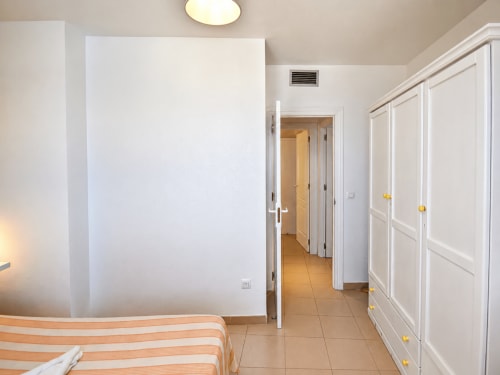 Dormitorio con cama de rayas, armarios blancos y puerta al pasillo en apartamento El Calón Playa, Cuevas del Almanzora