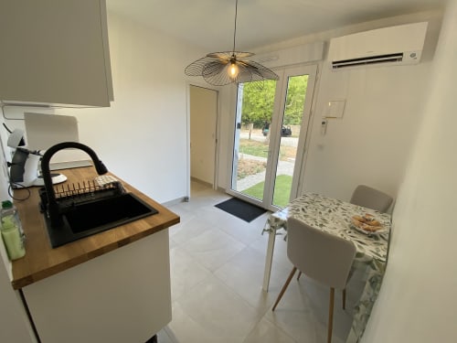 Kitchenette moderne avec évier noir, plan de travail en bois, table à manger et portes donnant sur le jardin à La Maison Blanche