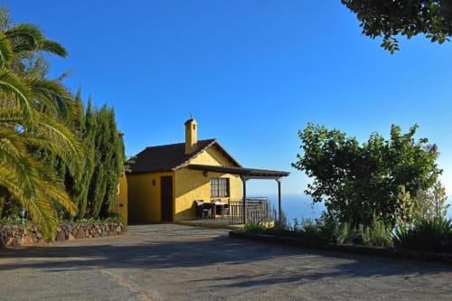 Villa amarilla con terraza vista al océano en Tijarafe, La Palma, rodeada de palmeras y jardines exuberantes