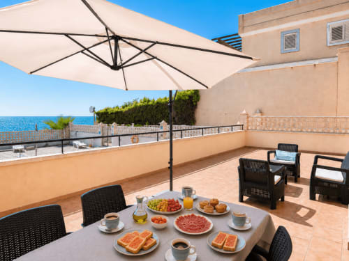 Beachfront terrace at Apartamentos El Calón Playa with sea view, shaded umbrella, dining setup, and Mediterranean coast in