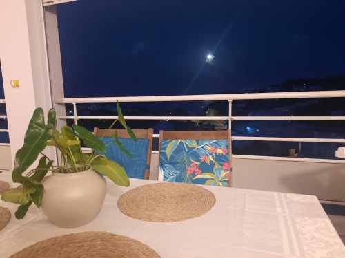 Terrasse dînante de l'appartement Kay Betty en Martinique avec vue mer, ciel nocturne éclairé par la lune, plante en pot et colorée