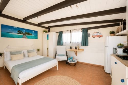 Chambre de la maison de Carlo à Corralejo avec lit, kitchenette, plafond à poutres, œuvre d'art turquoise et vue sur la mer