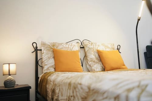 Chambre accueillante aux Maisons En Or Cayenne avec coussins moutarde, literie à motifs et lampe de chevet décorée