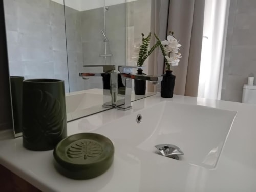 Salle de bains moderne chez Laure & Marc avec lavabo blanc, robinetterie chromée, accessoires verts et orchidée décorative