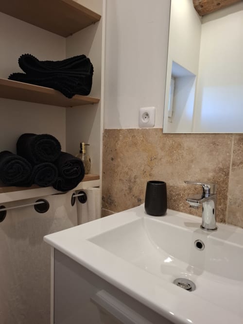 Lavabo moderne avec robinetterie chromée, serviettes noires sur étagères en bois, dosseret en carrelage beige, miroir au-dessus du lavabo chez