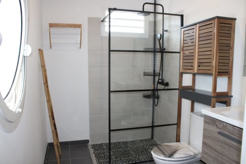 Salle de bains moderne à Maisons En Or à Cayenne avec douche à paroi noire, toilettes et meuble de rangement en bois
