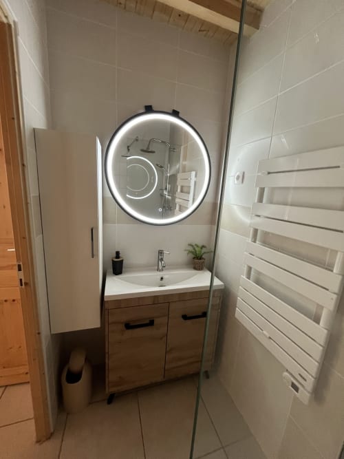 Salle de bain moderne du gîte Le Papillon au Cocon De Curson avec miroir circulaire lumineux, meuble vasque en bois et carrelage blanc