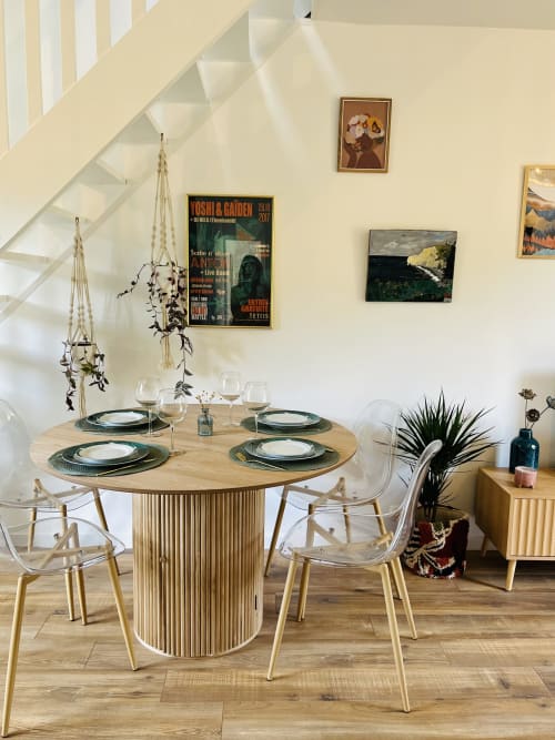 Salle à manger moderne du gîte d'Étretat avec table ronde en bois, chaises transparentes et vue sur le jardin sous l'escalier