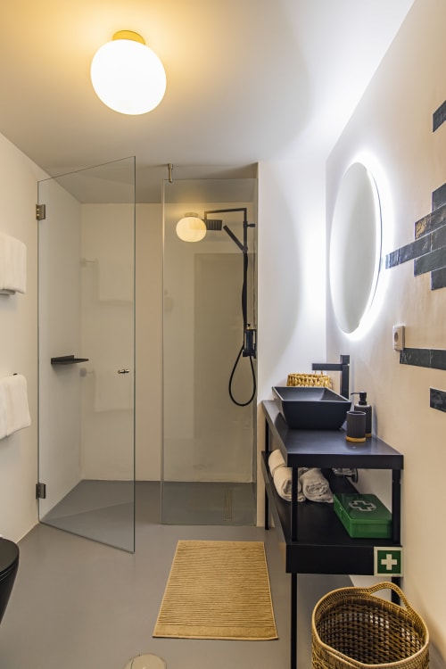 Modern bathroom in Porto hotel with walk-in shower, black vanity, illuminated mirror, and gold accents