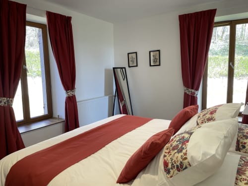 Chambre élégante au Château de Vaux Mordan avec accents bourgogne, literie crème, portes-fenêtres donnant sur le jardin