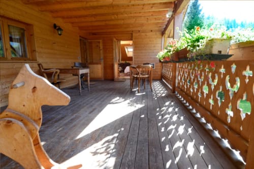 Terrasse ensoleillée en bois à l'Auberge Nemoz avec vue sur les montagnes, balustrade décorée, plantes en pots et mobilier rustique