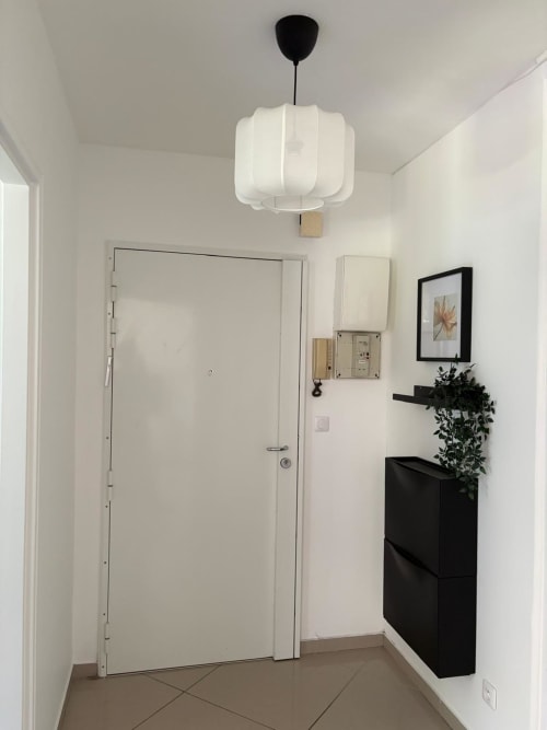 Entrée contemporaine de l'appartement Le Paradis Des Logis à Pierrefitte-sur-Seine avec porte blanche, luminaire suspendu et meuble noir