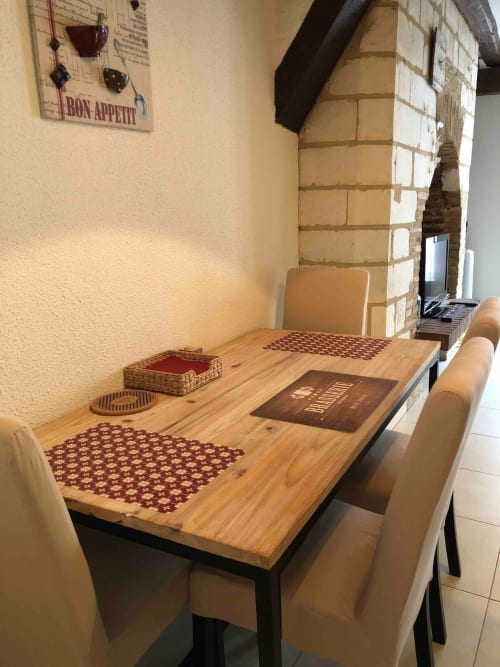 Coin repas cosy de l'appartement Le Charmant Zola à Troyes avec table en bois, chaises beiges et murs en briques apparentes.