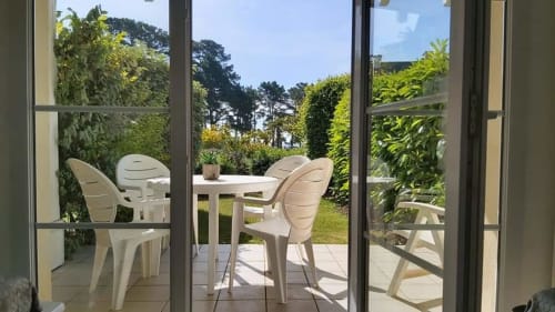 Furnished patio with white chairs and table overlooking garden at Ô CAP COZ apartment in La Fôret-Fouesnant, Brittany