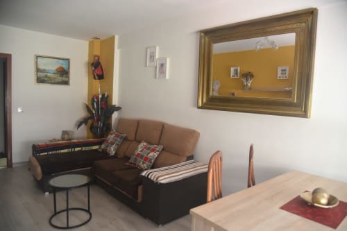 Bright living room in Benavente apartment with brown sofa, wooden table, and framed mirror on yellow accent wall