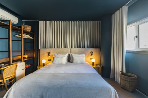 Quarto moderno em hotel no Porto com paredes verde-azulado, iluminação dourada na cabeceira, roupa de cama branca e móveis contemporâneos.