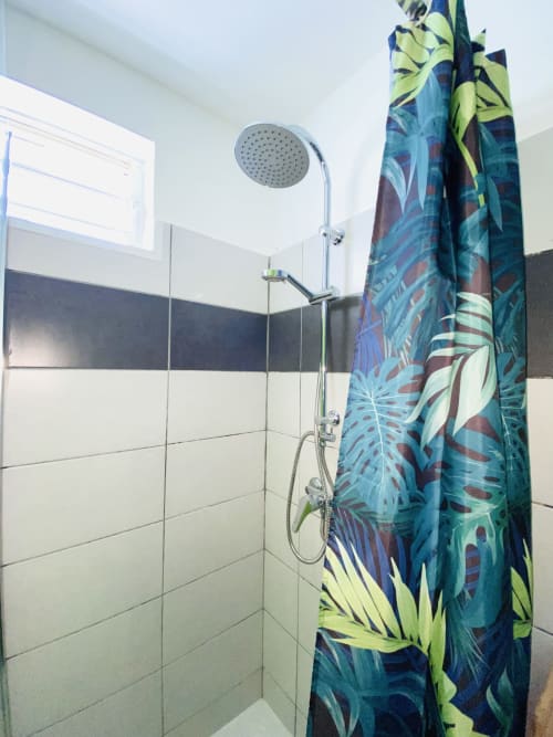 Salle de bain moderne avec pommeau de douche pluie et rideau tropical coloré dans l'appartement T3 de Maisons En Or, Cayenne