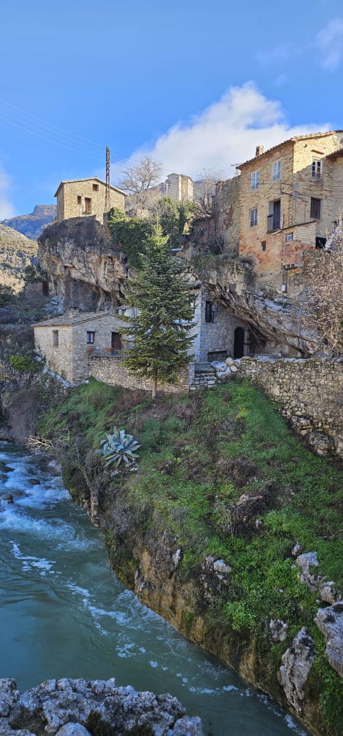 Edificios de piedra encaramados en acantilados cubiertos de musgo sobre un río turquesa en las montañas Prepirineo de Montgat