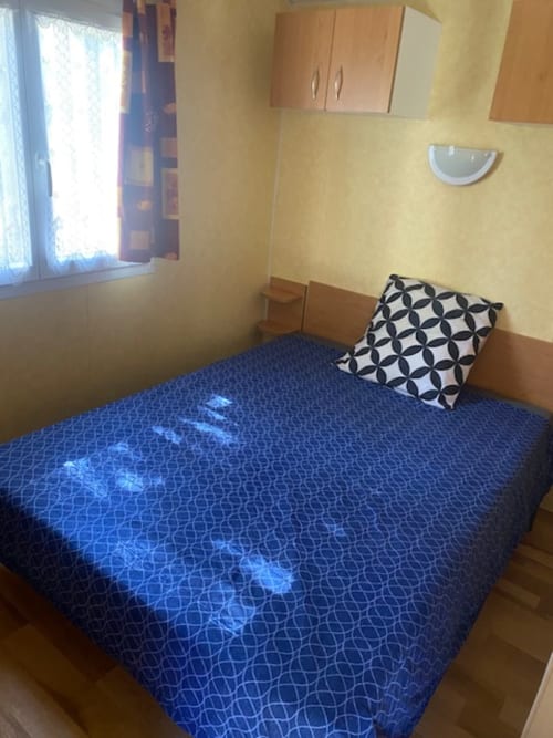 Chambre cosy du mobil-home Auvergne au Relais de La Mirpe, Bergerac avec literie à motifs bleus et oreiller géométrique