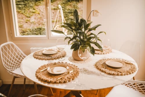 Ensemble de table à manger ronde moderne avec sets de table tressés, couverts et plante en pot au cottage ART DE VOYAGER à Étretat