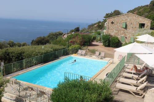 Resort pool with sea view at Résidence Roc E Mare in Cargèse, Corsica. Loungers, umbrellas, and Mediterranean coastline