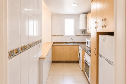 Cocina de galera moderna con muebles de madera, electrodomésticos blancos y azulejos decorativos en Apartamentos El Calón Playa, Cuevas